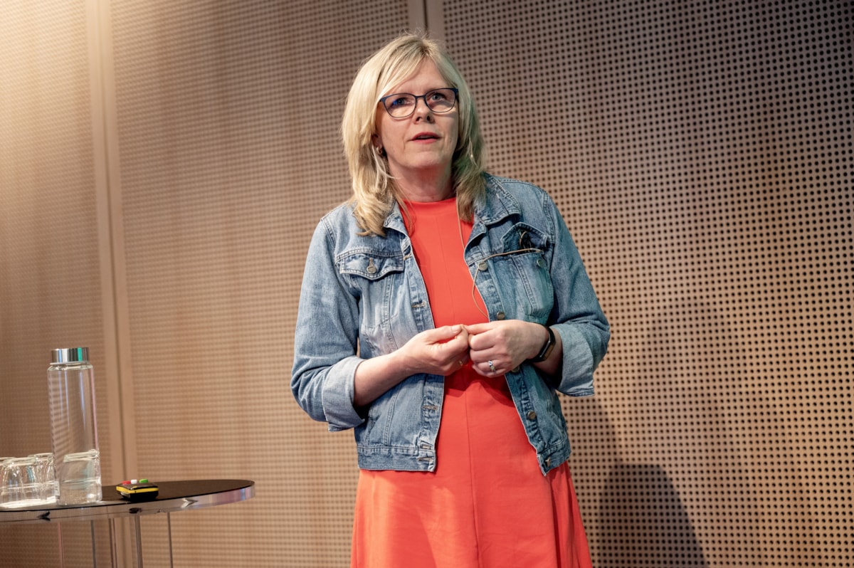 Tove Iversen står på scenen i en rød kjole og snakker til Fagkonferansens publikum.