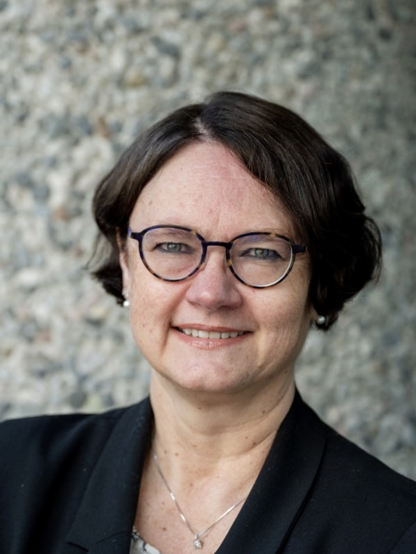Portrett av Solveig Jensveen foran en vegg i naturbetong.
