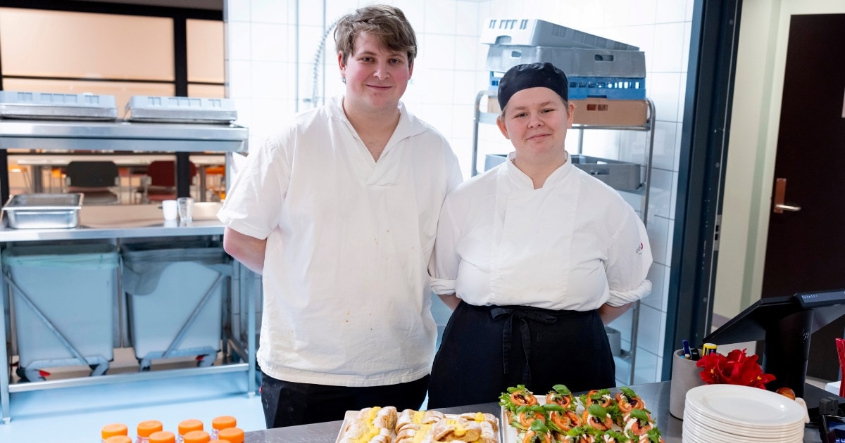 To unge mennesker i kokkeuniform på et kjøkken med et fat fullt av delikate smørbrød foran seg.